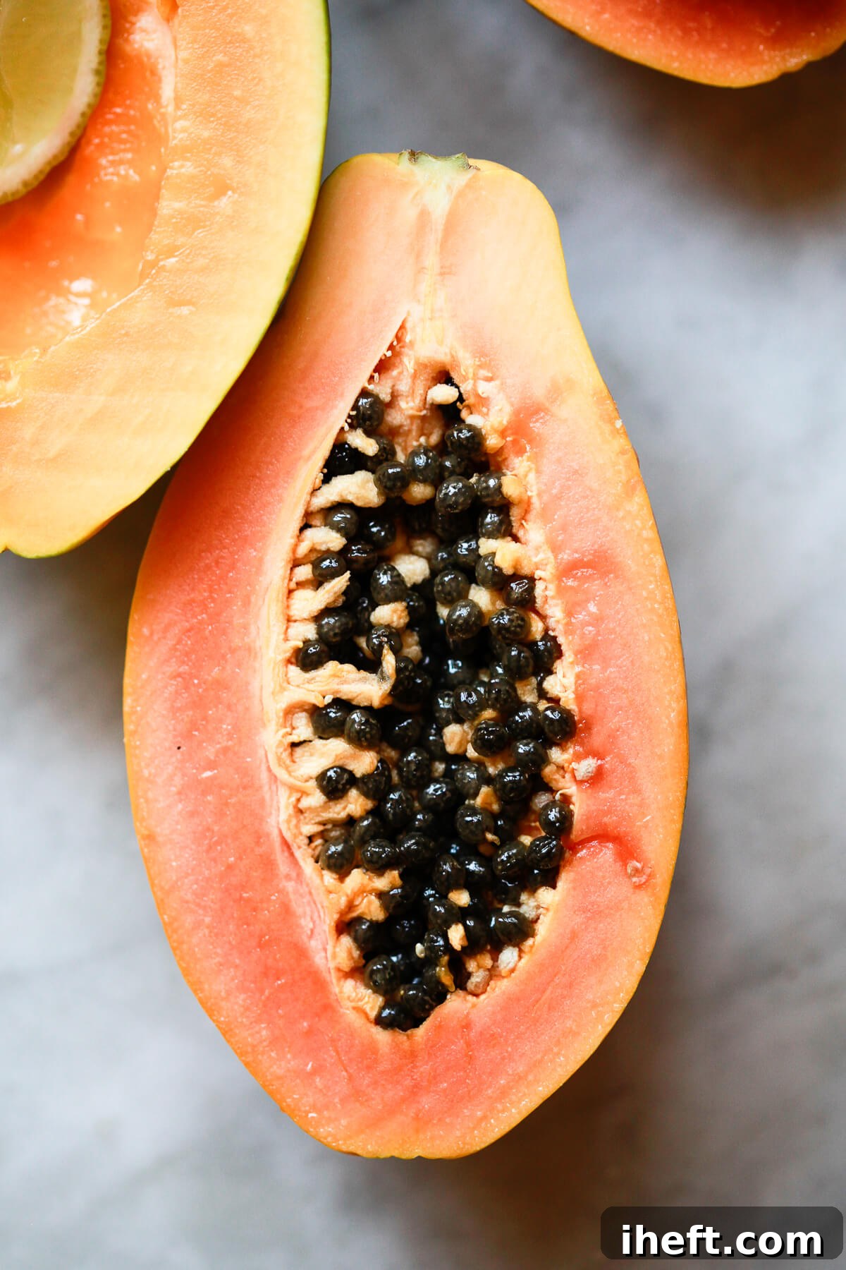 Half a papaya filled with its characteristic black, glistening seeds, sitting on a pristine marble countertop, ready for preparation.