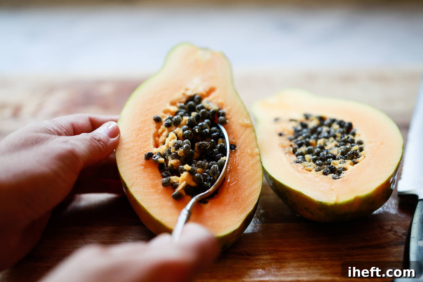 A spoon meticulously scoops out the dark seeds from the center of a Hawaiian papaya half.