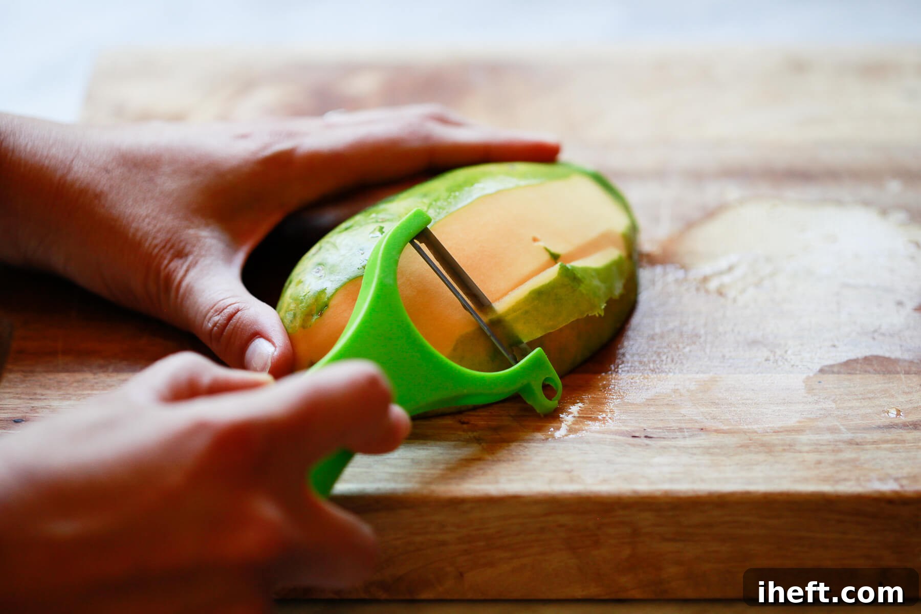 A green vegetable peeler glides effortlessly along the skin of a papaya, removing its outer layer.