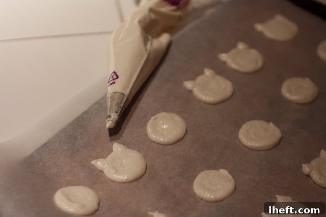 Freshly piped Hello Kitty macaron shells on parchment paper