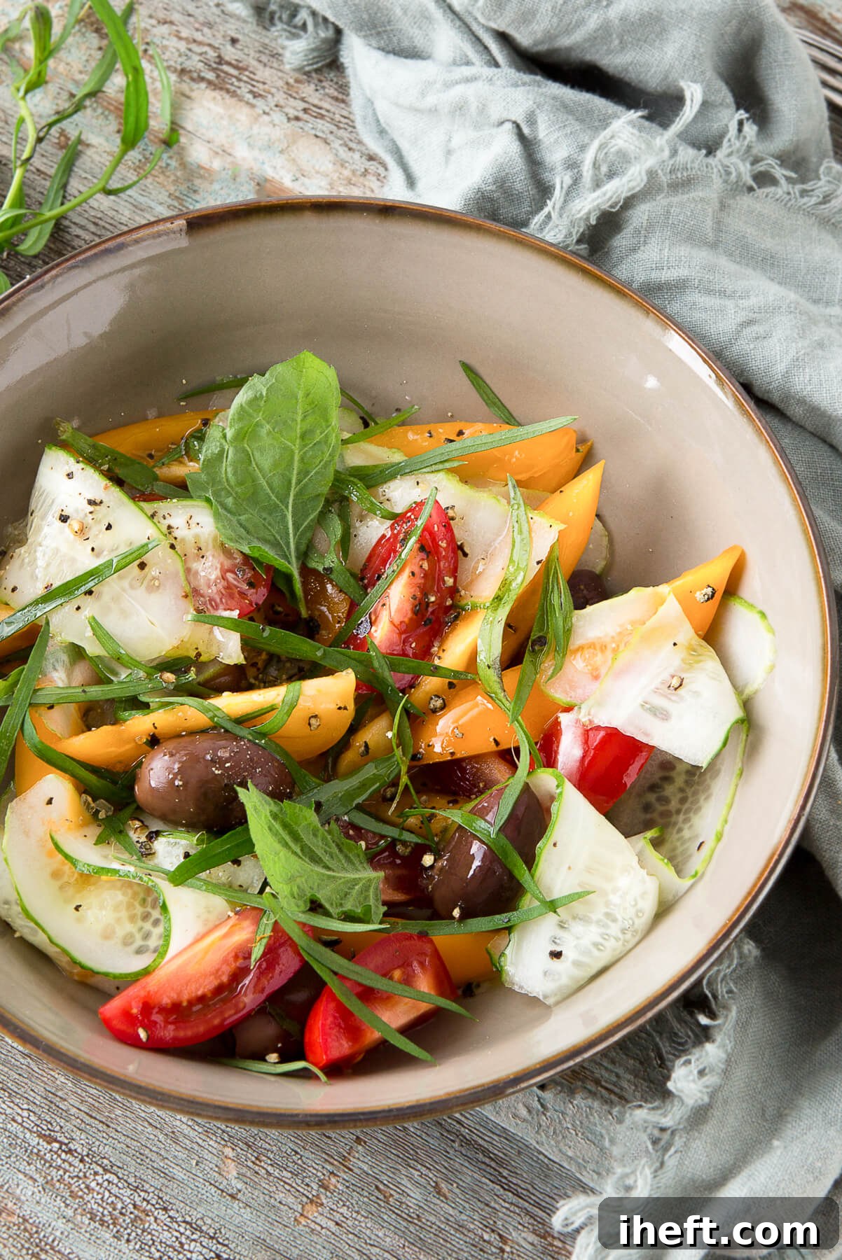 A bowl of salad with cucumber, tomatoes, olives, and tarragon.