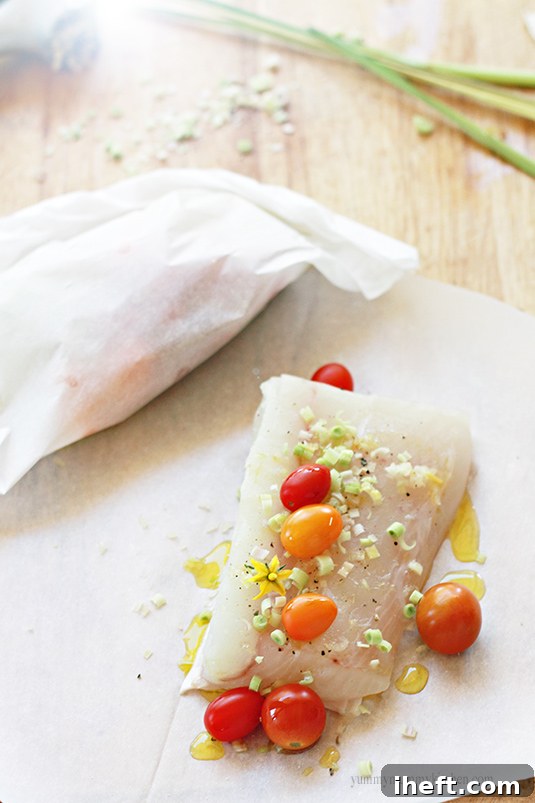 A piece of raw halibut with minced lemongrass, vibrant cherry tomatoes, and fresh herbs, arranged on parchment paper, ready for baking.