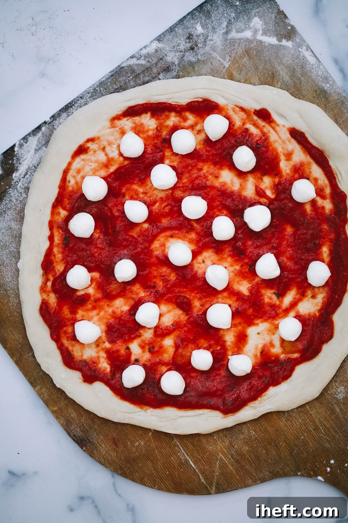 An overhead photo of an uncooked pizza on a pizza peel, ready for the Ooni oven. 