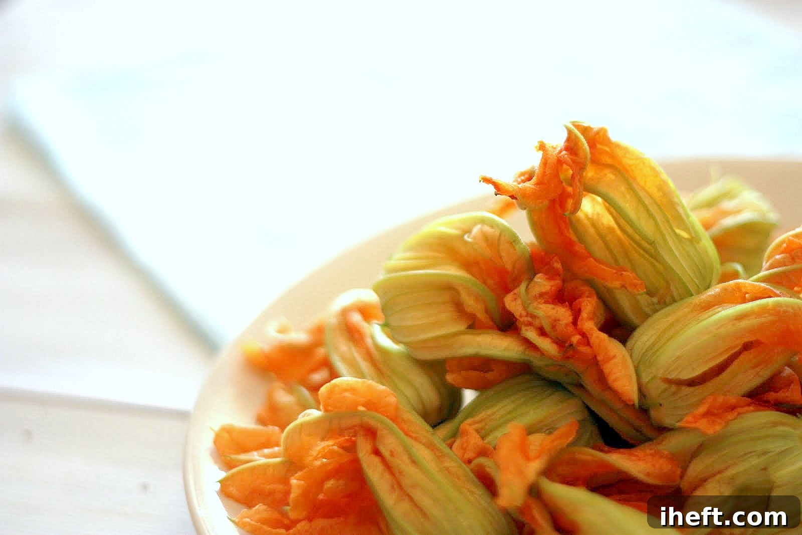 A beautiful ceramic bowl generously filled with freshly picked, vibrant yellow and orange squash blossoms, ready for cleaning and cooking.