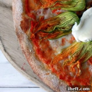 Close-up of a rustic Squash Blossom Pizza with vibrant yellow blossoms, melted cheese, and a crispy crust, photographed from above and ready for enjoyment.