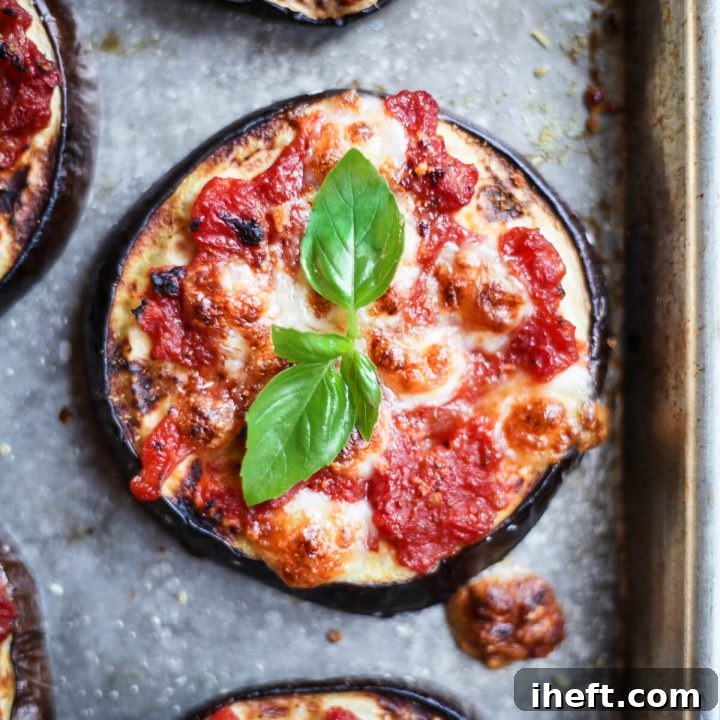 An overhead close-up photo of a mini eggplant pizza round topped with tomato sauce, cheese, and basil.