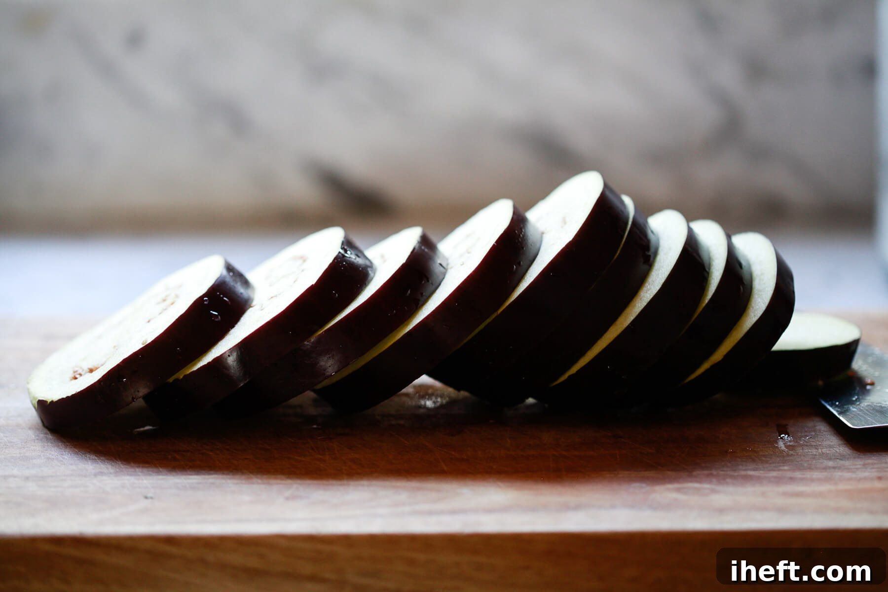 A globe eggplant is sliced into rounds on a wooden cutting board.