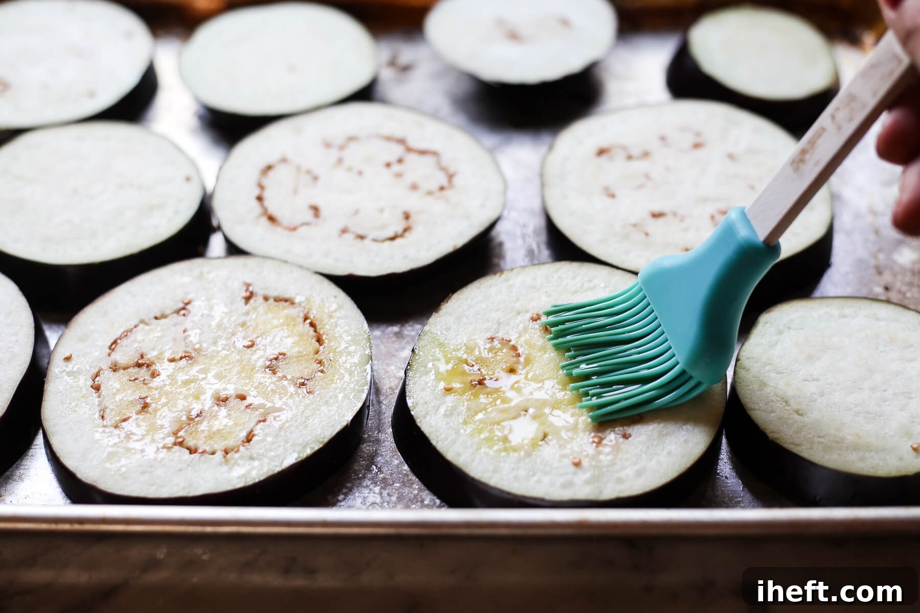 Olive oil is brushed onto eggplant rounds with a blue pastry brush.