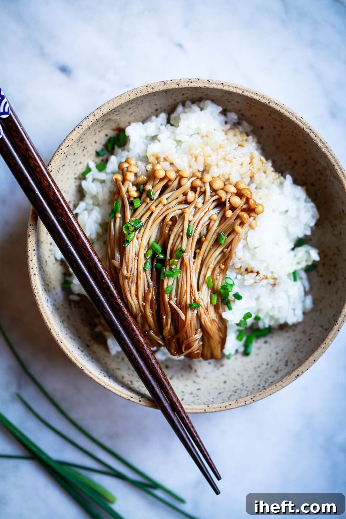 An overhead photo of Enoki mushroom with teriyaki sauce over a bed of rice and topped with black sesame seeds and chives.