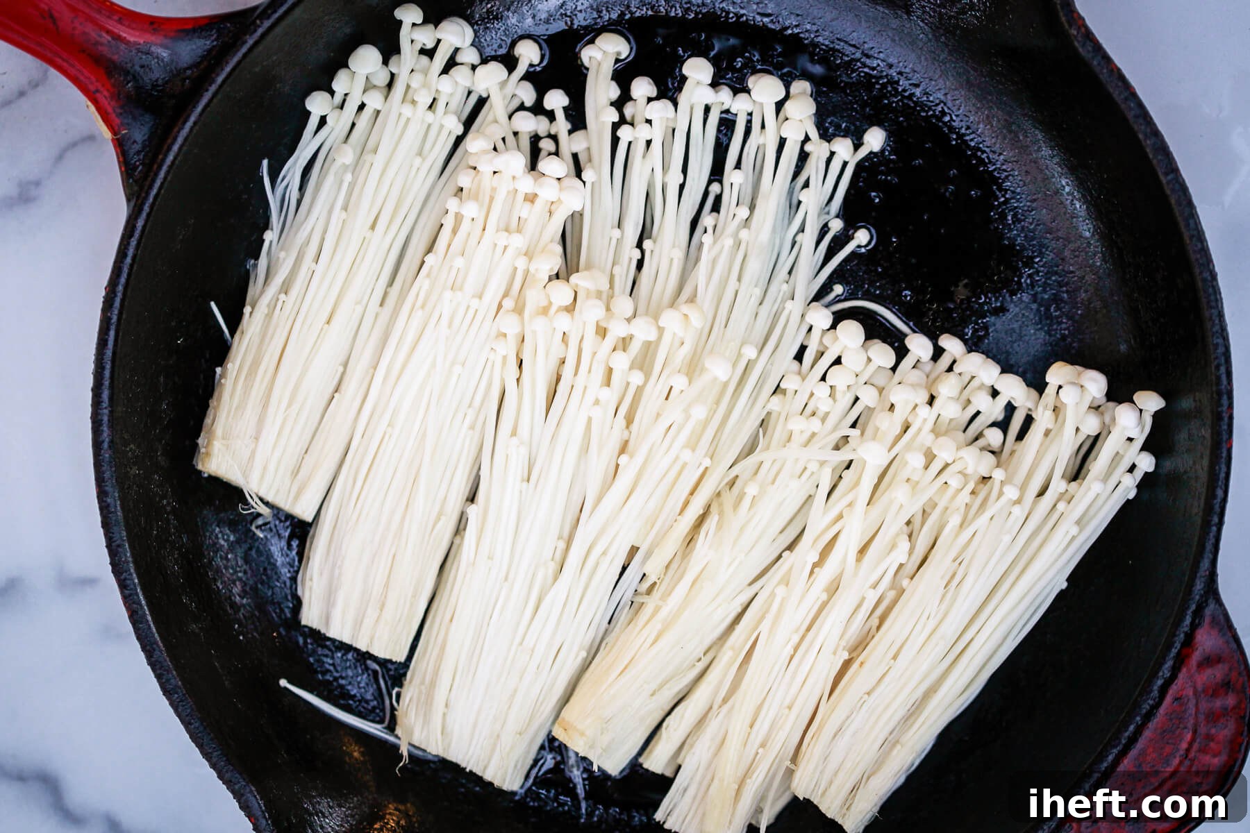 Enoki mushrooms cook in oil in a cast iron skillet.