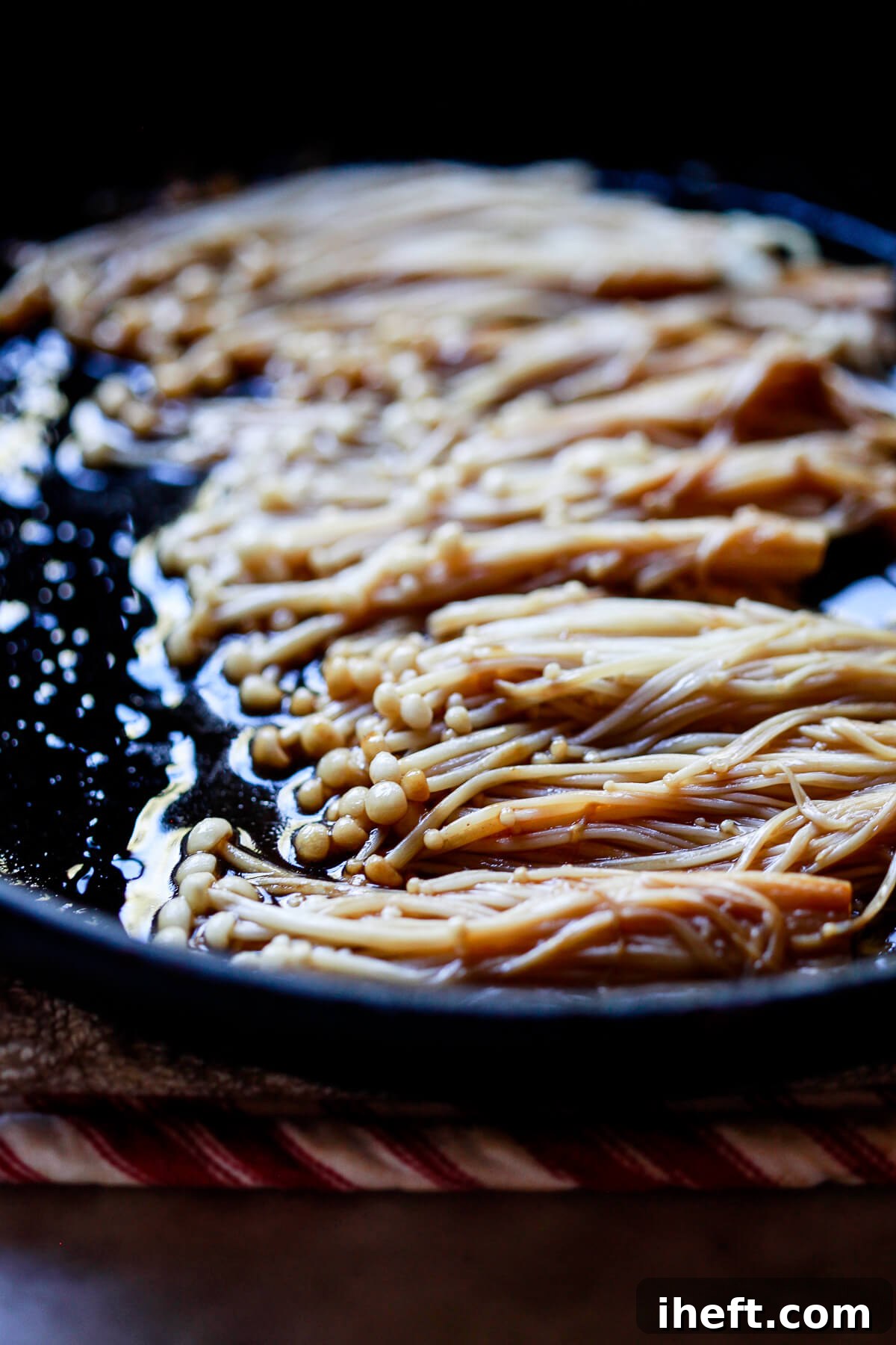 Enoki mushrooms cook in soy sauce and teriyaki sauce in a cast iron skillet.