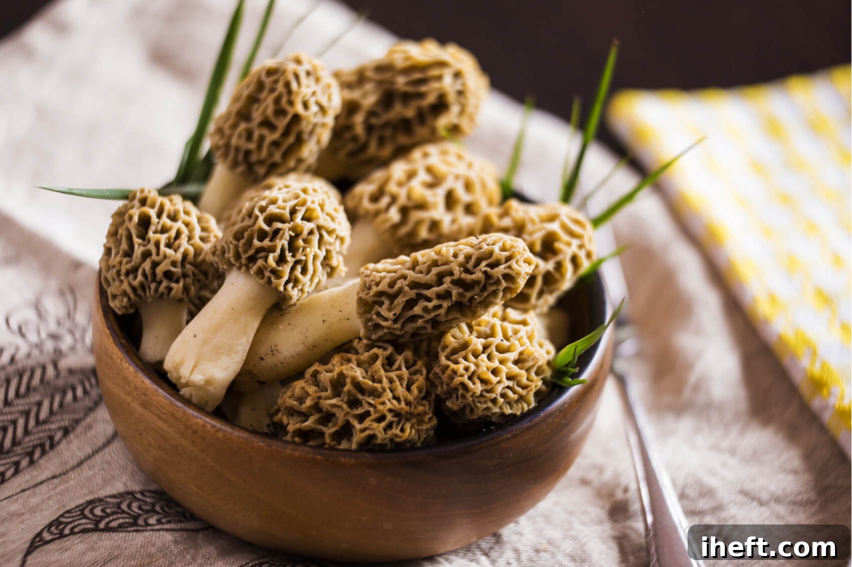 A small wooden bowl filled with fresh, intricately textured morel mushrooms, highlighting their unique appearance.