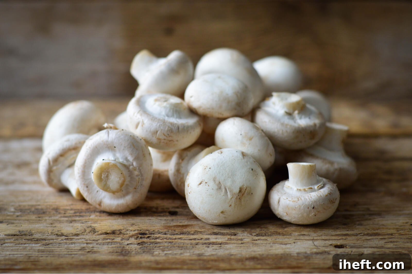 A generous pile of fresh white button mushrooms neatly arranged on a rustic wooden cutting board, ready for preparation.