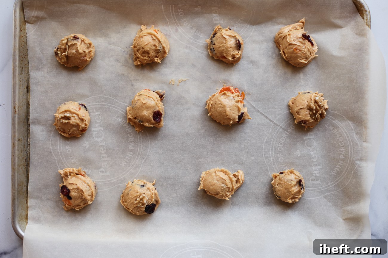 Portioned scoops of persimmon cookie dough are neatly arranged on a parchment-lined baking sheet, ready to be baked into delicious fall treats.