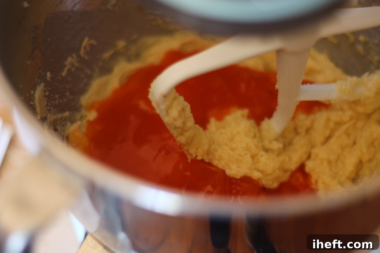 Translucent persimmon pulp being added to the creamed butter, sugar, and egg mixture in a mixing bowl, ready to be incorporated into the cookie dough.