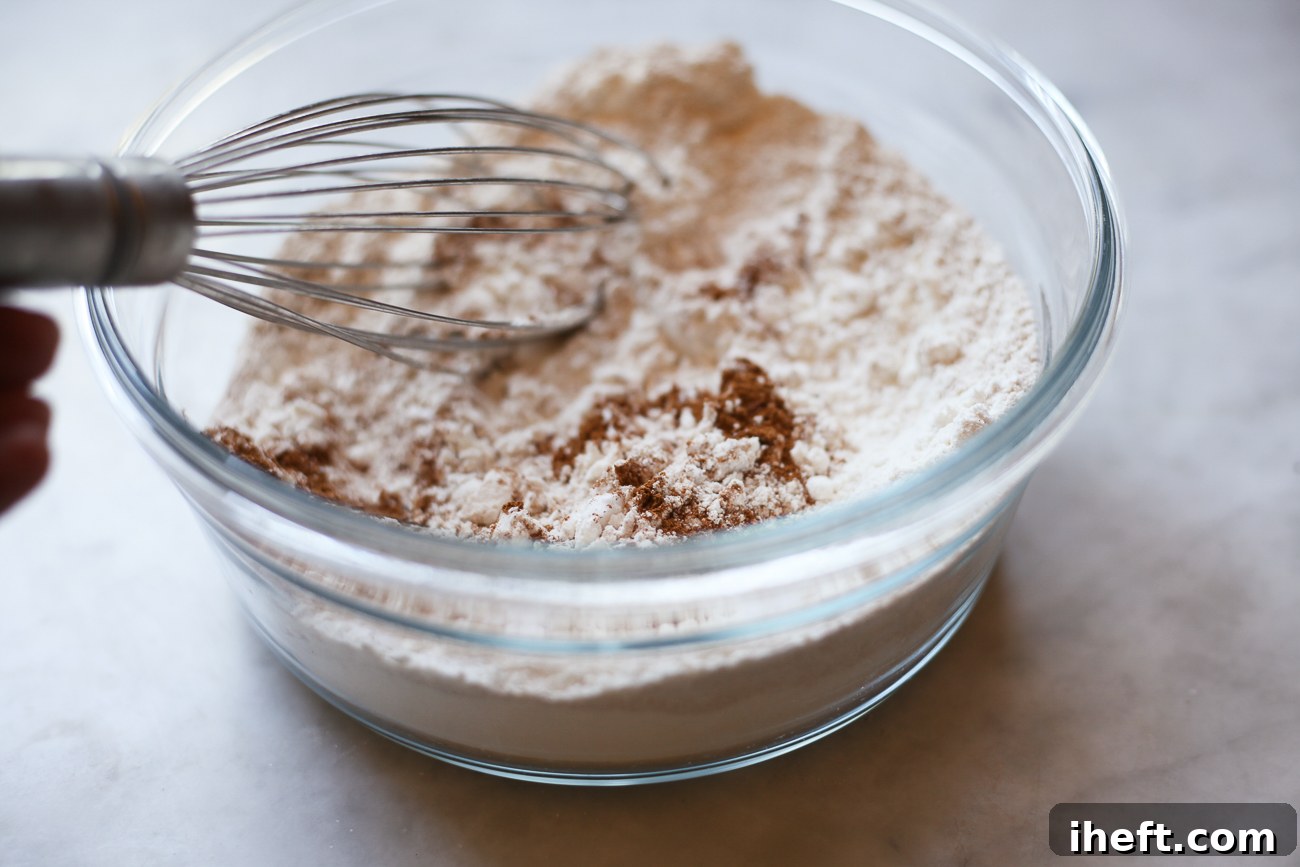All-purpose flour, baking soda, and ground cinnamon are whisked together in a clear glass bowl, preparing the dry ingredients for the persimmon cookie dough.