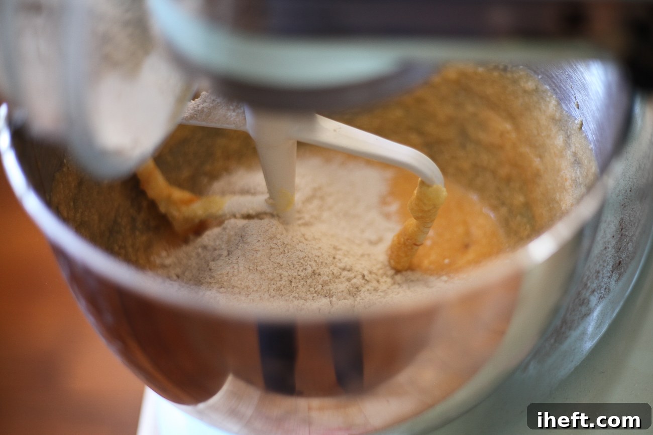 The dry ingredients are being carefully added to the wet mixture in a stand mixer, beginning the process of forming the persimmon cookie dough.