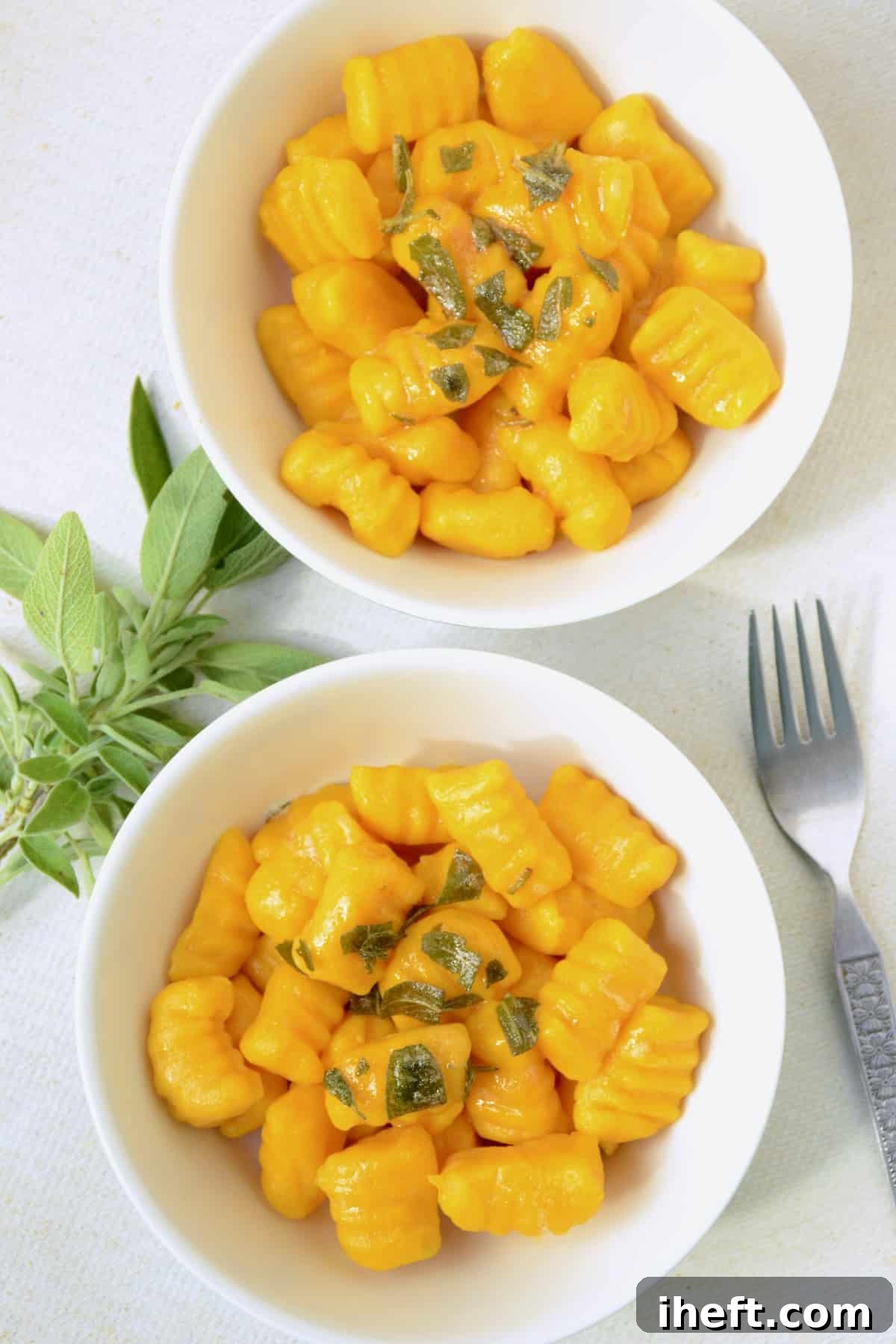 An overhead photo of two white bowls filled with pumpkin gnocchi garnished with sage. 