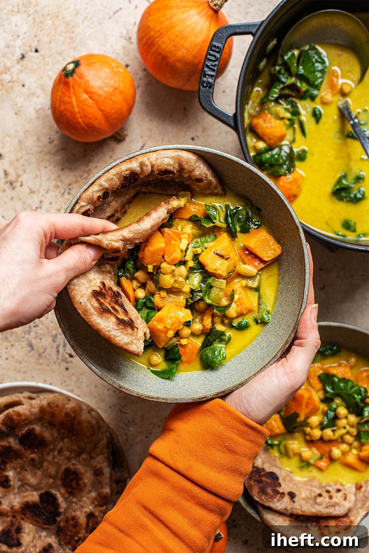 A woman's hands scoop up some pumpkin chickpea curry with a piece of flatbread from a ceramic bowl. 