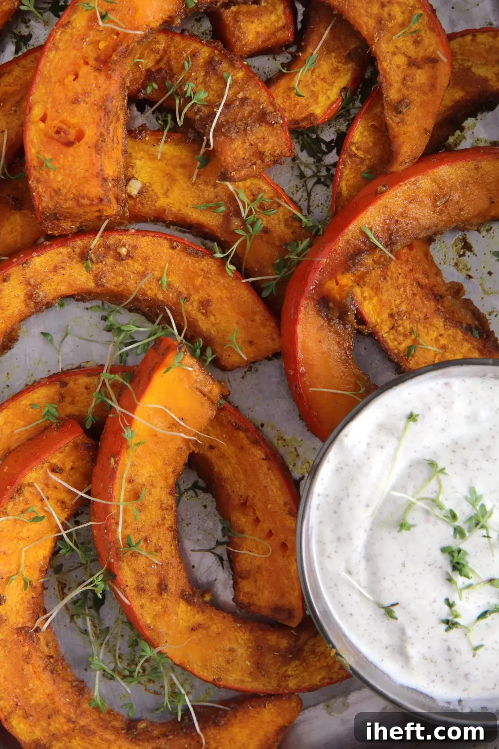 Wedges of roasted pumpkin on a cookie sheet are topped with micro greens. A small dish of white yogurt dip sits in the lower right corner. 