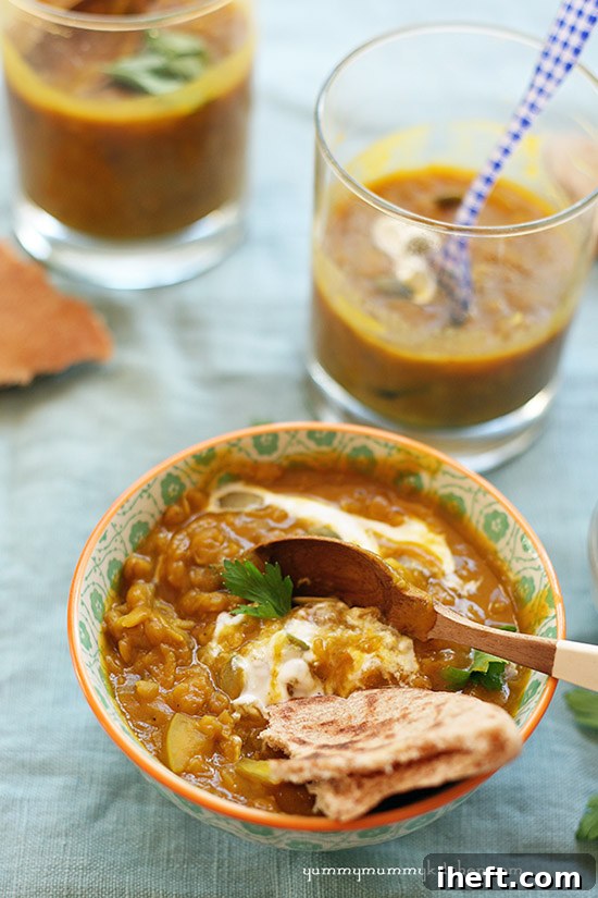Three small bowls of pumpkin lentil soup topped with yogurt and pita bread. 