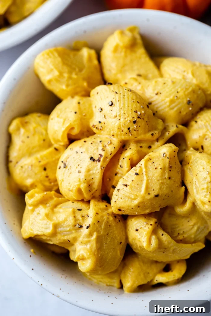 A close-up overhead photo of pumpkin mac and cheese shells in a small white bowl garnished with black pepper. 