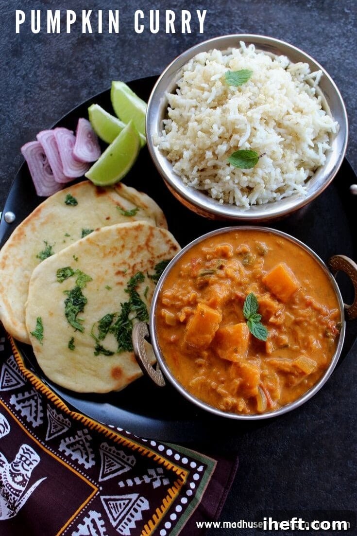 A bowl of pumpkin Indian curry sits on a black round tray next to white rice, naan bread, lime wedges, and red onions.. 