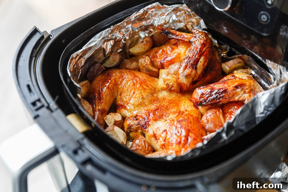 An open air fryer basket lined with a small amount of aluminum foil, containing chicken pieces and potatoes.