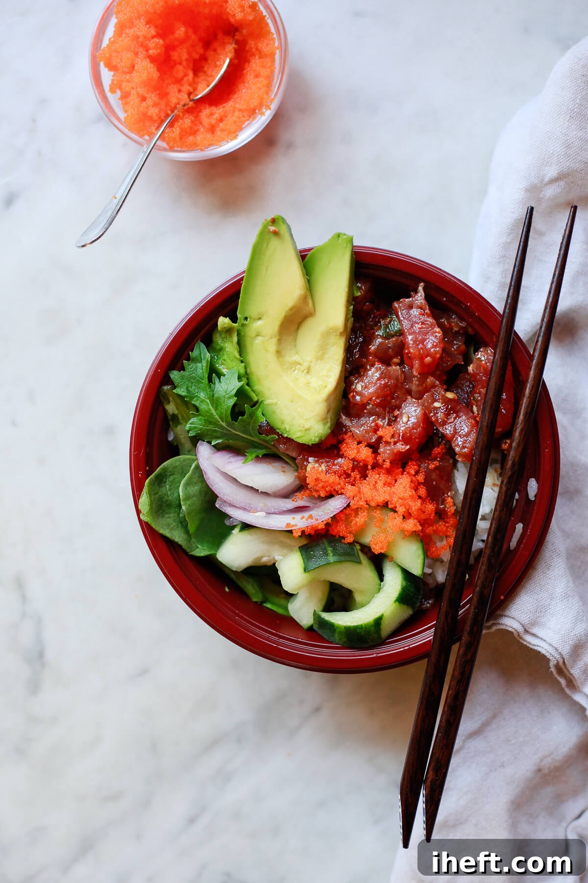 An overhead view of a vibrant Hawaiian poke bowl, generously filled with cubes of fresh ahi tuna, crisp cucumber, mixed greens, creamy avocado, and iridescent massago (capelin roe), creating a colorful and healthy meal.