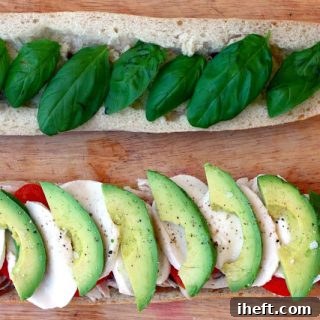 A perfectly assembled Caprese sandwich on a baguette, showcasing layers of avocado, tomato, fresh mozzarella, and basil, drizzled with balsamic glaze.