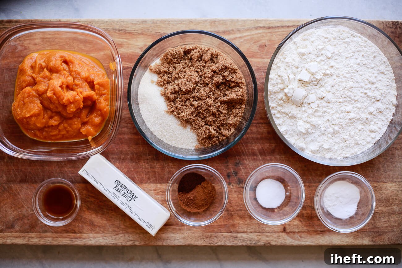 The ingredients for vegan pumpkin cookies are neatly arranged in bowls on a rustic wooden cutting board, ready for baking. 