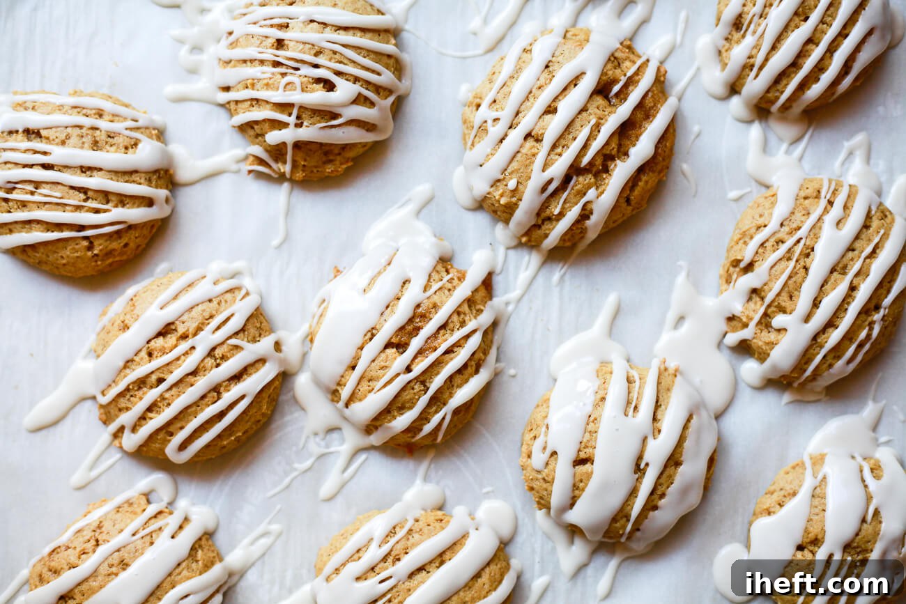 Vegan pumpkin cookies drizzled with white icing are perfectly arranged on a parchment-lined cookie sheet, ready to be enjoyed.
