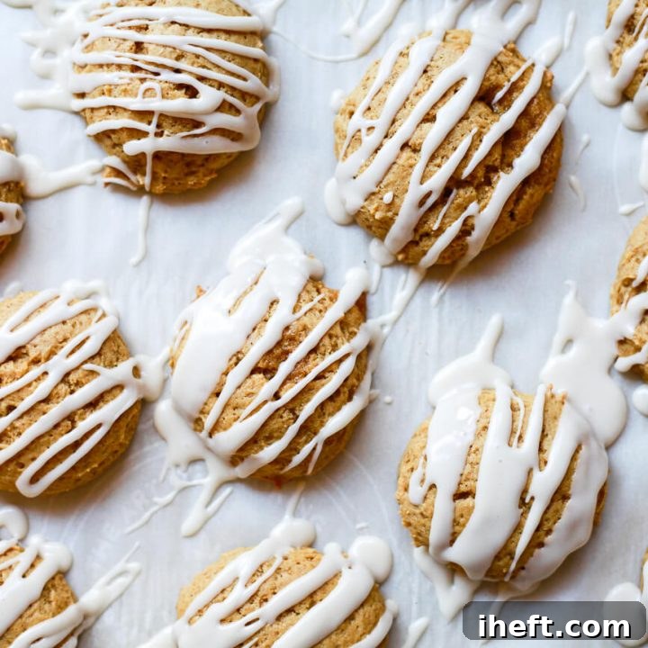 Vegan pumpkin cookies drizzled with white icing on a parchment lined cookie sheet.