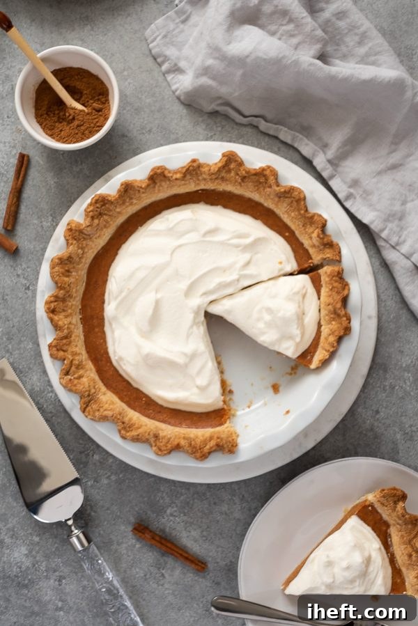A rustic pumpkin pie with a golden, slightly uneven crust, topped generously with a voluminous, pillowy mound of freshly whipped cream, with one slice already removed.