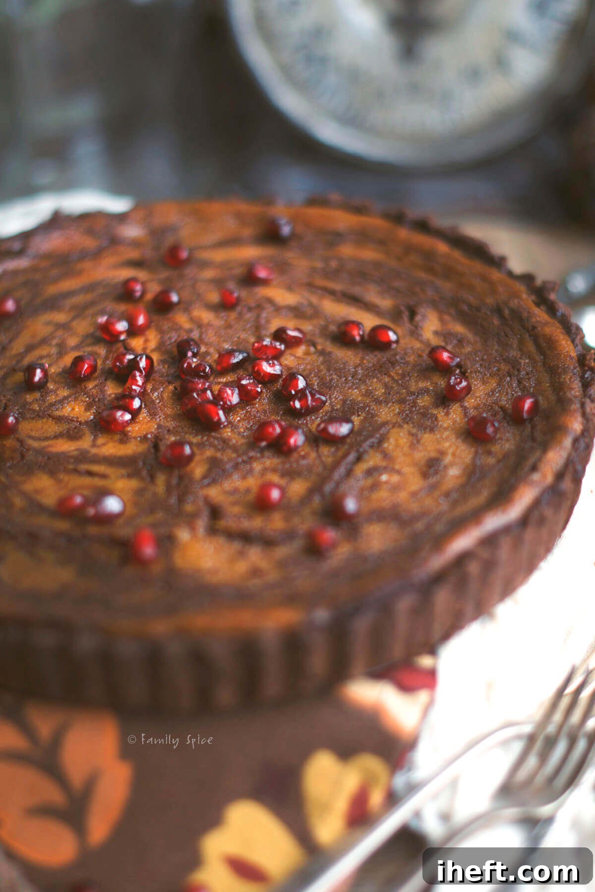 A double chocolate pumpkin pie topped with a vibrant sprinkle of red pomegranate arils, highlighting the rich, dark chocolate crust and filling.