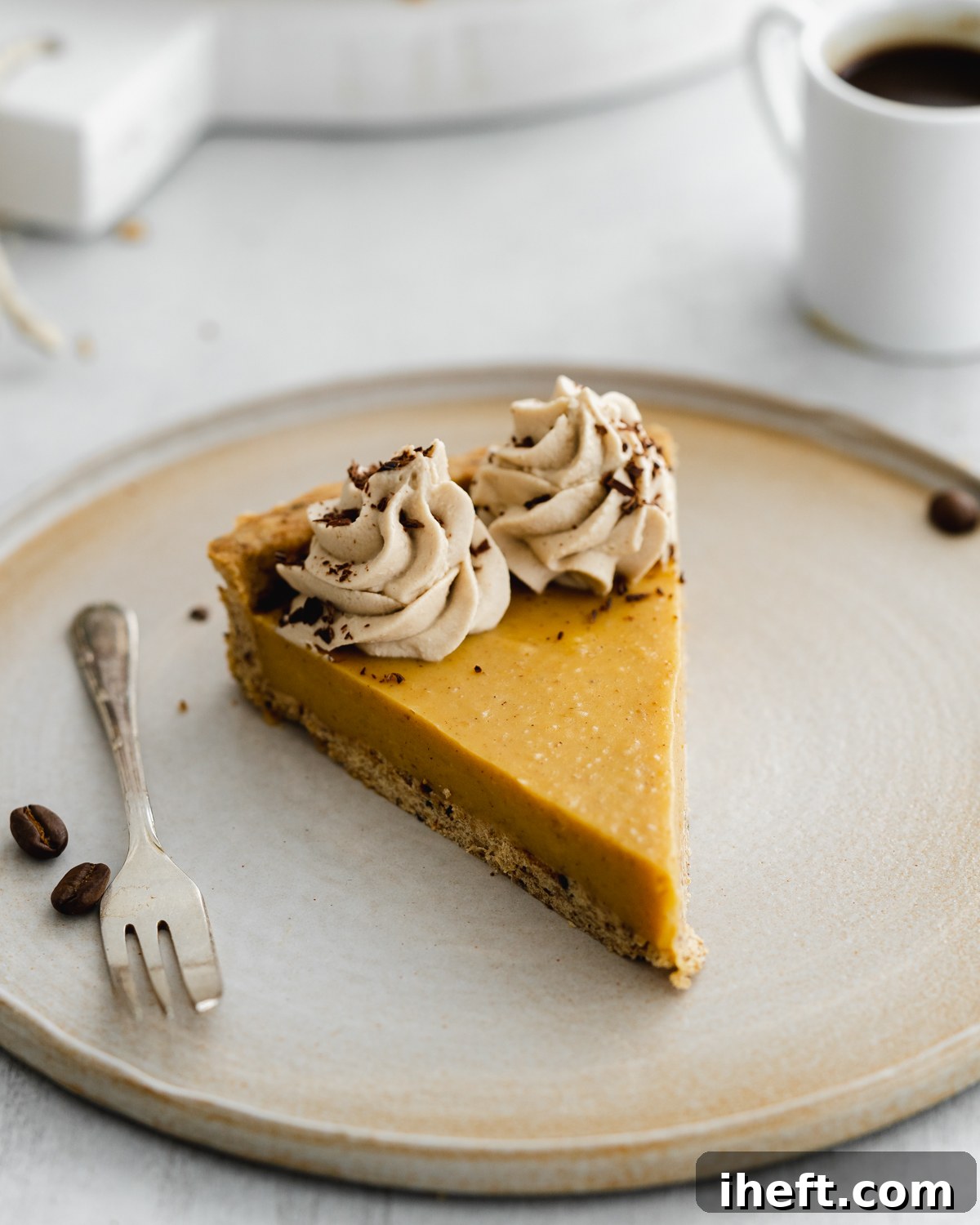 A single slice of pumpkin pie on a ceramic plate, elegantly adorned with intricate swirls of piped coconut whipped cream, lightly dusted with coffee powder for a sophisticated finish.