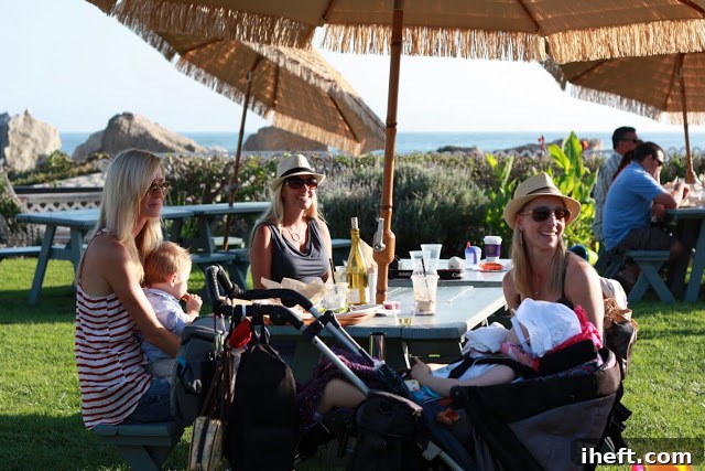Group of smiling mothers enjoying a relaxed meal outdoors at Padaro Beach Grill with their children playing nearby.