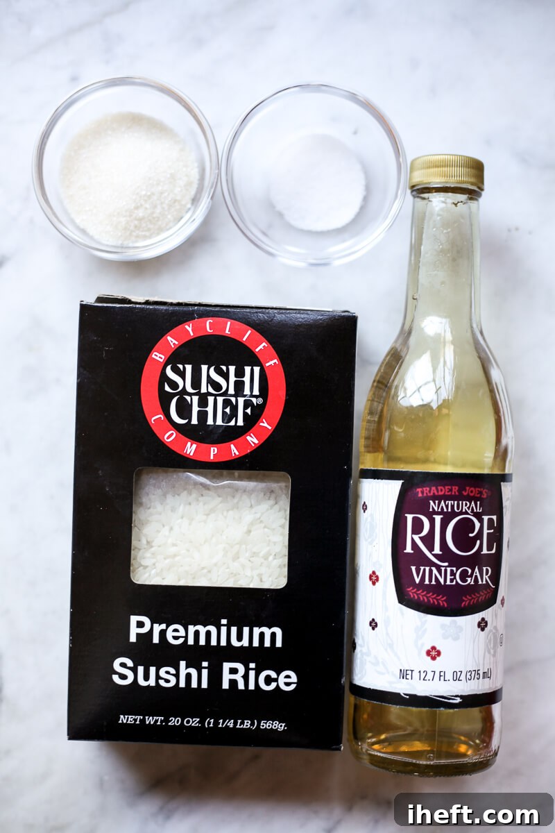 Ingredients for making sushi rice are neatly arranged on a sleek marble countertop: a bowl of cooked white rice, a bottle of clear rice vinegar, a small dish of salt, and a small dish of sugar, showcasing the essentials for traditional sushi preparation.