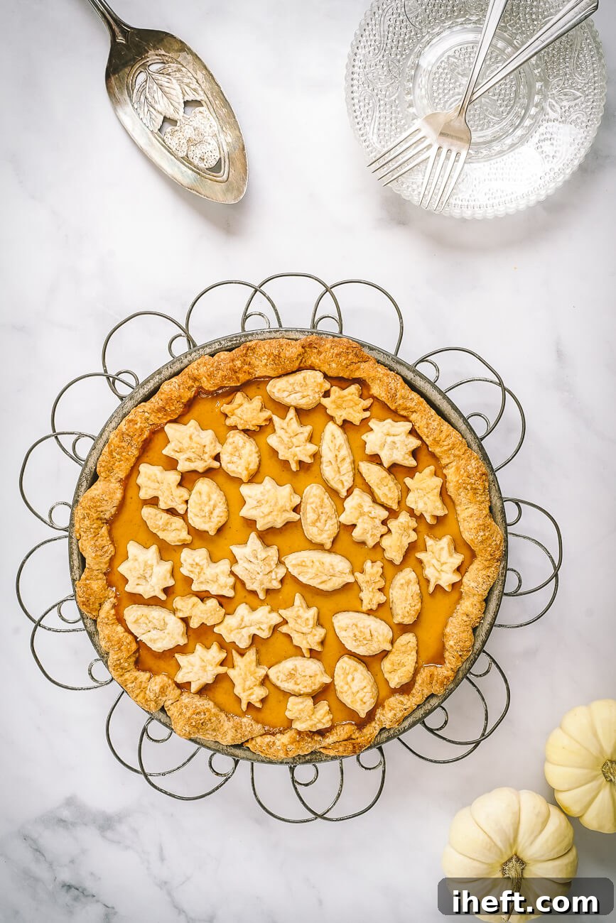 A beautiful pumpkin pie decorated with fall pastry leaves on a white marble counter. 