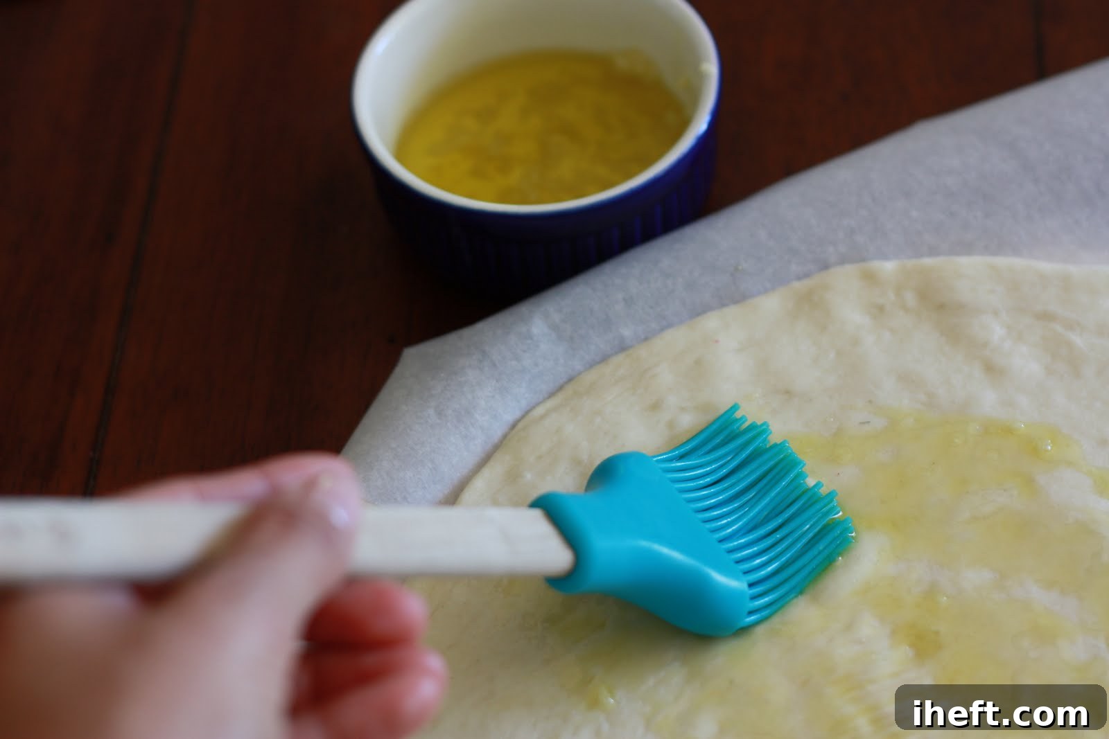 A perfectly prepared homemade pizza dough, round and smooth, is being expertly brushed with a rich, aromatic garlic-infused olive oil, ready for its delicious toppings. The golden surface hints at a perfectly crisp base.