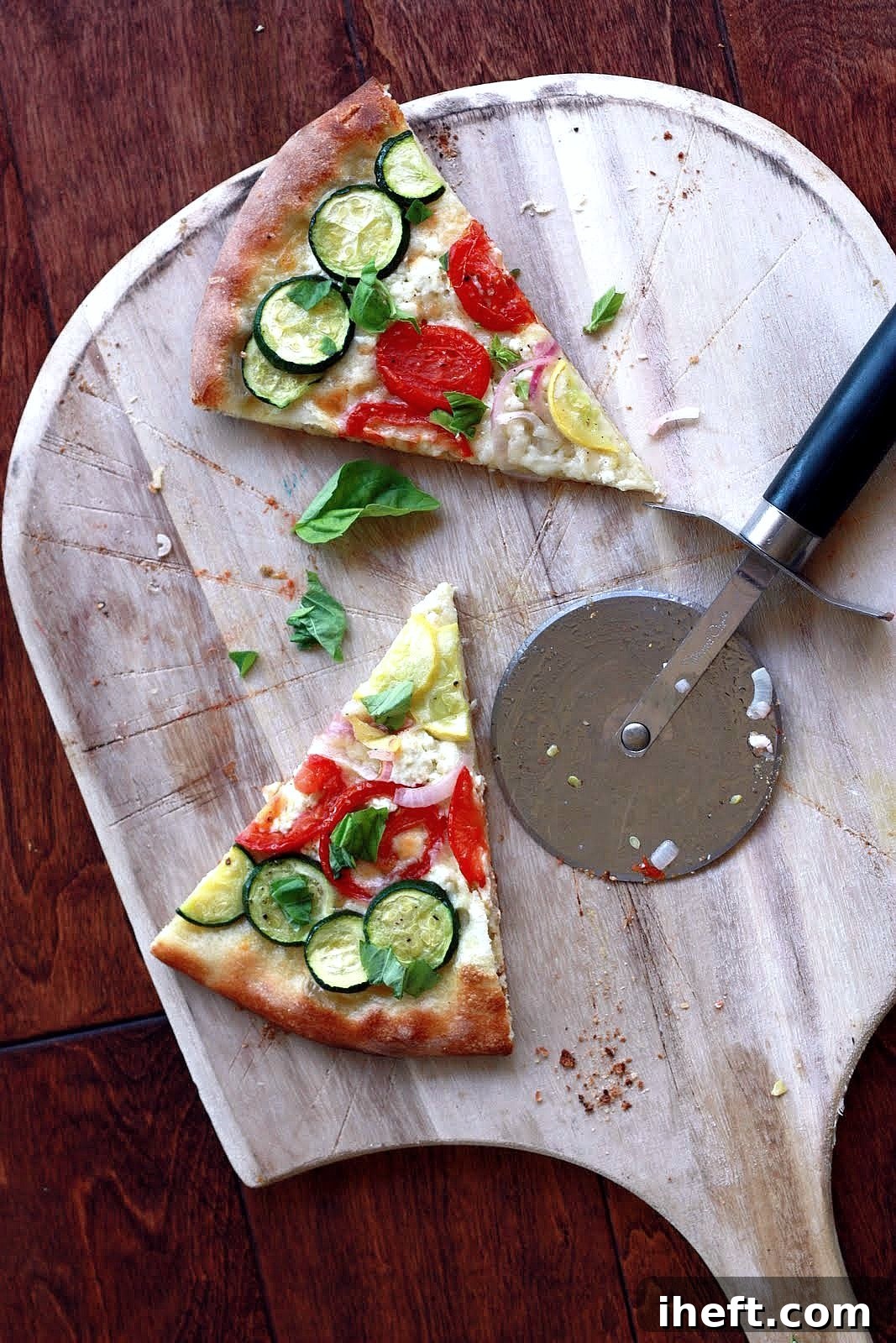 Two perfectly baked slices of rainbow vegetable pizza, adorned with fresh basil leaves, are elegantly presented on a classic wooden pizza peel, ready to be served and enjoyed. The crust appears golden and crisp, while the colorful vegetables are tender and vibrant.