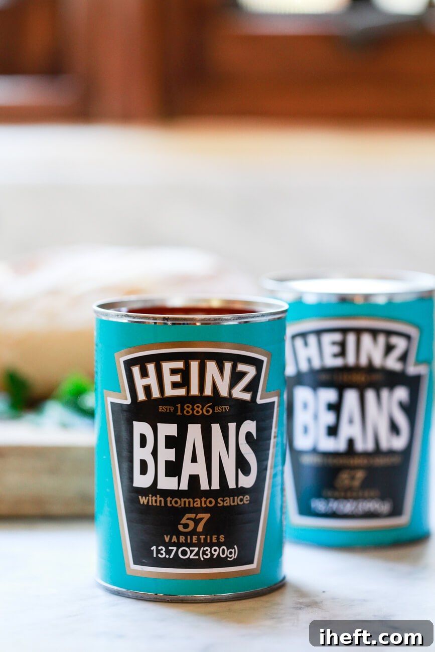 Two cans of British Heinz beans with tomato sauce on a marble countertop. These beans have turquoise wrappers and are the type used as breakfast beans in the uk and for beans on toast. 
