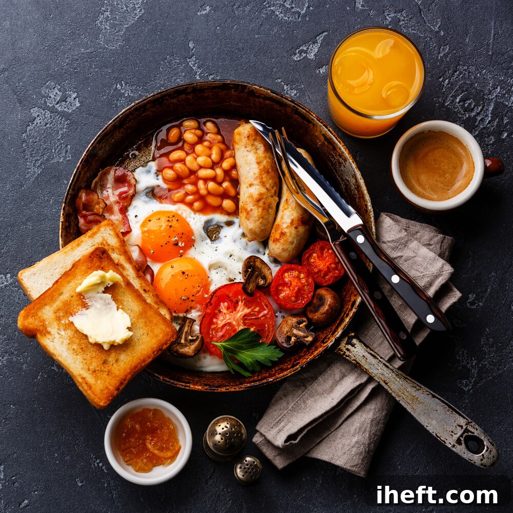 An overhead photo of a full English breakfast including beans, toast, eggs, tomatoes, and sausage served in a skillet. 