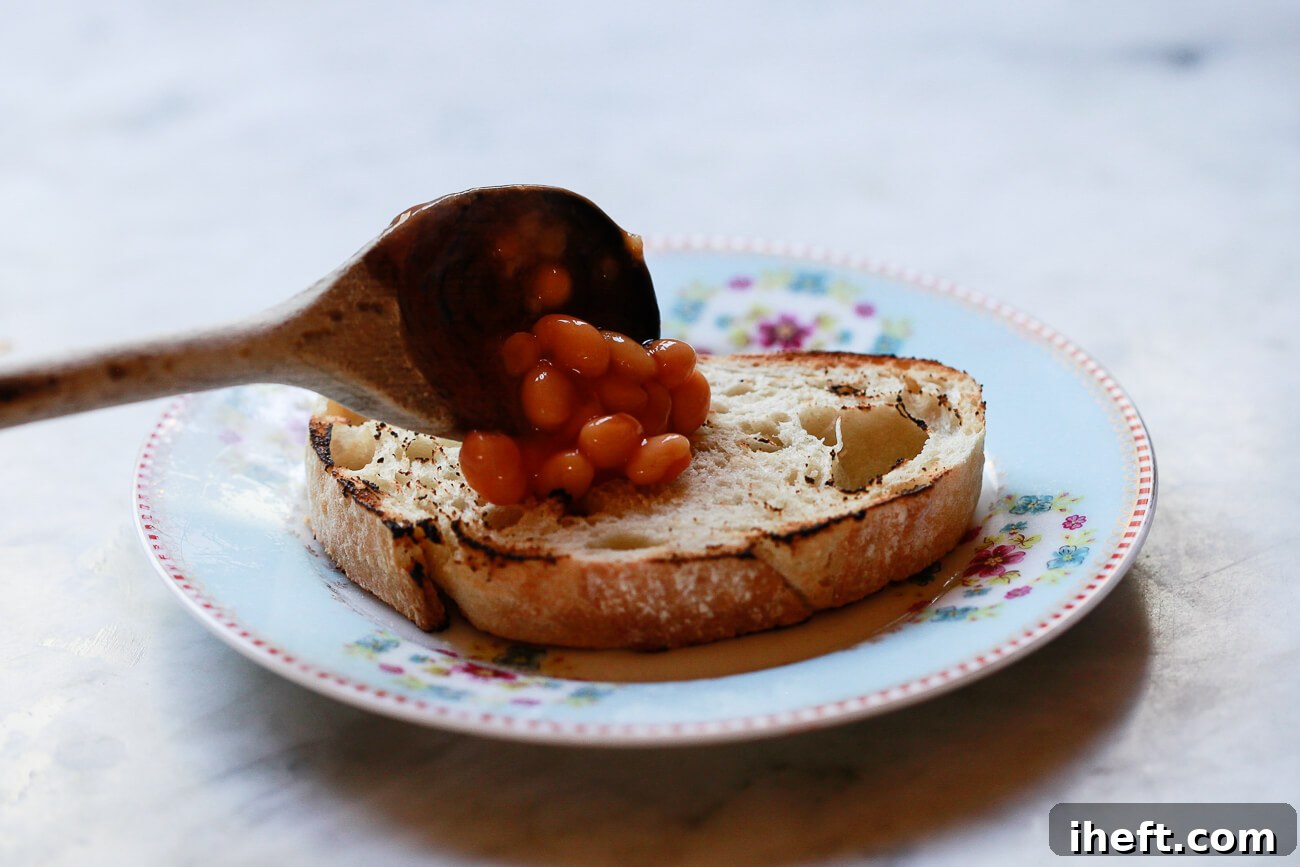 Heinz beans in tomato sauce is spooned onto a slice of toast with a wooden spoon.