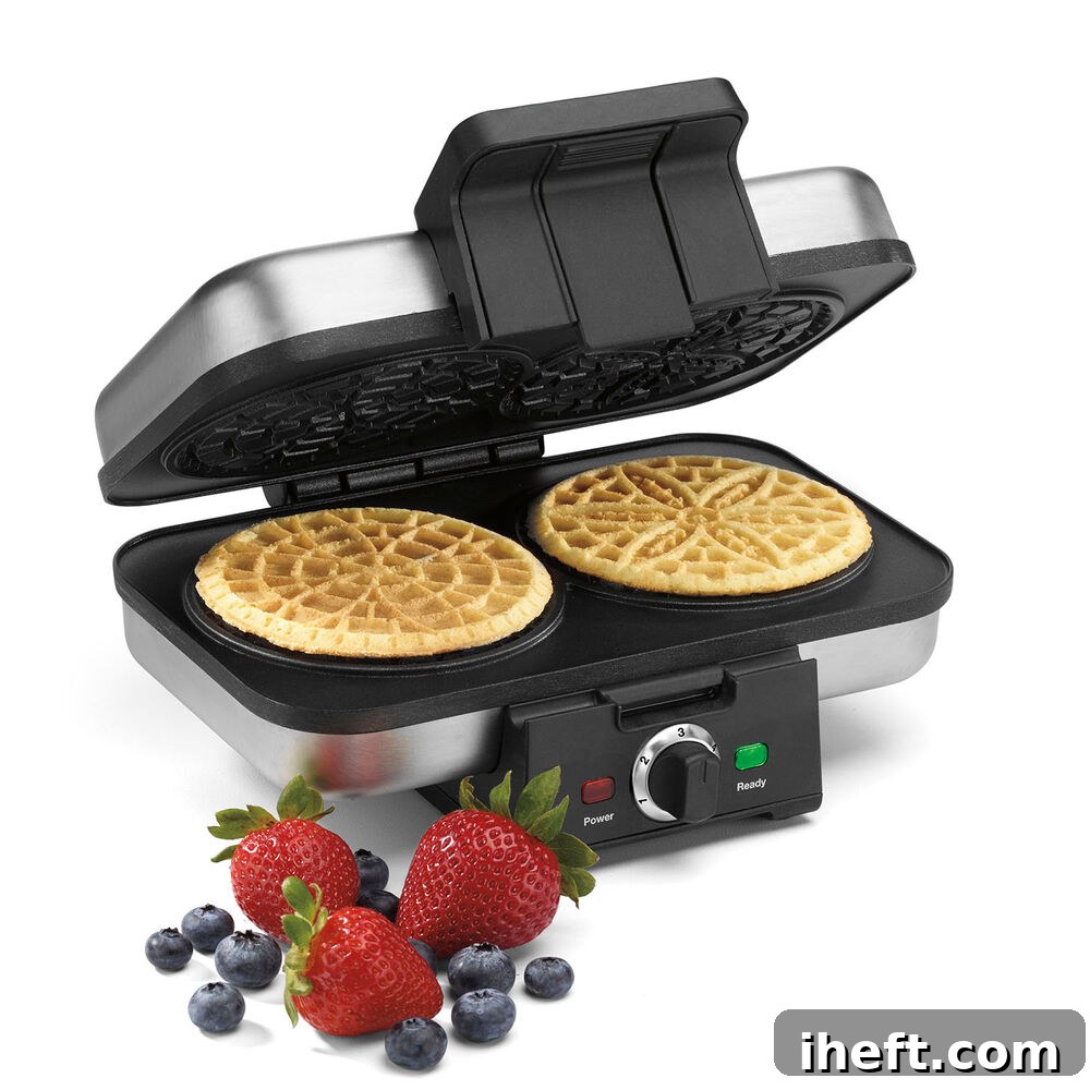 A Cuisinart pizzelle maker in action, cooking two perfectly round pizzelle cookies. Fresh berries are visible in the foreground.