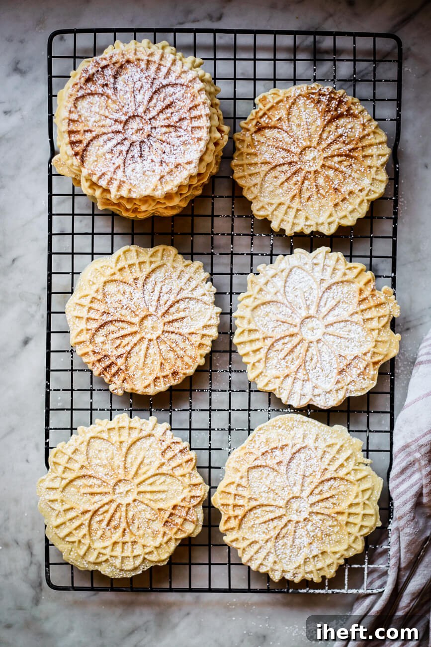Pizzelle cookies dusted with powdered sugar on a cooling rack on a marble countertop, ready to be enjoyed.