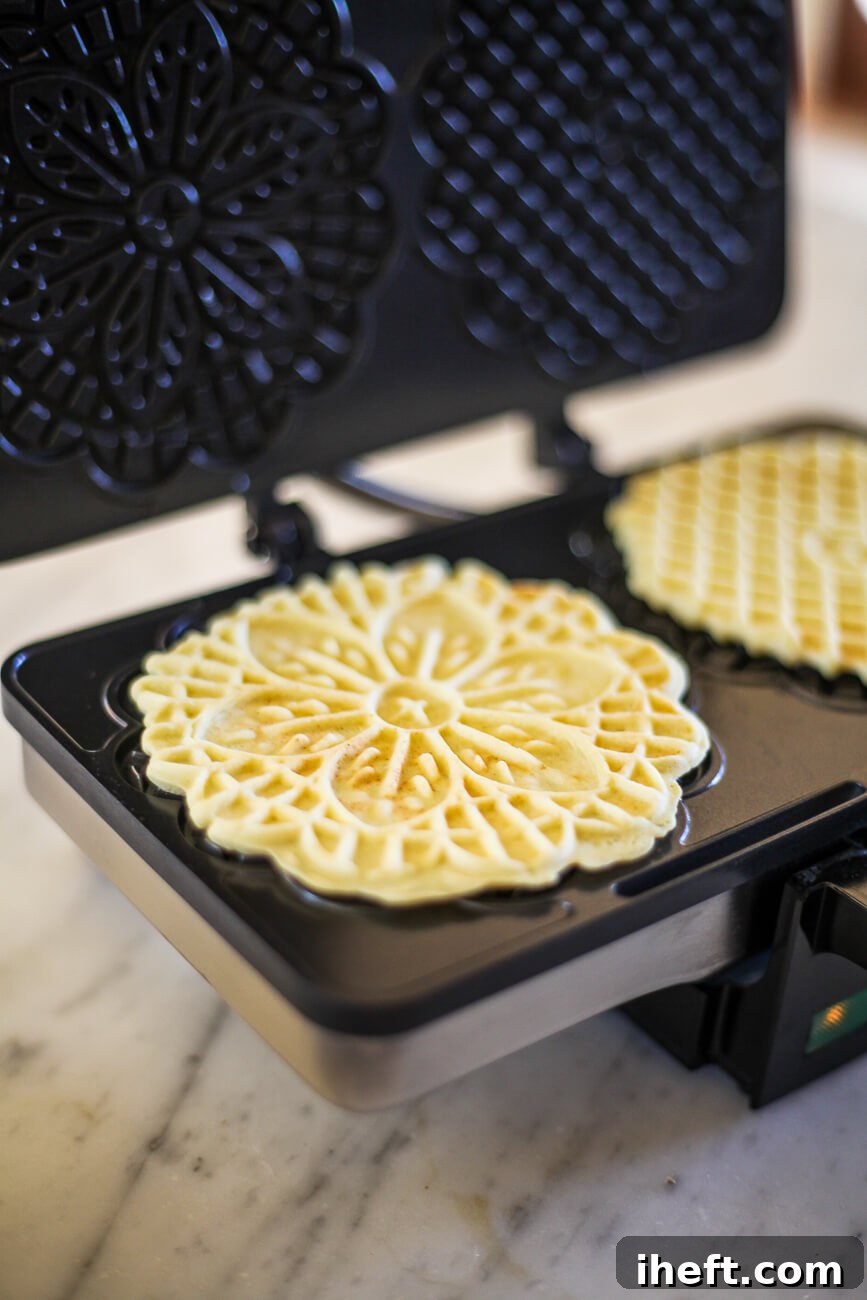 An opened pizzelle maker revealing two freshly baked, golden-brown pizzelle cookies with intricate patterns.