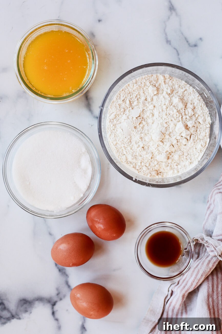 The essential ingredients for pizzelle cookie recipe laid out on a white marble countertop, including melted butter, flour with baking powder, sugar, three eggs, and vanilla extract.