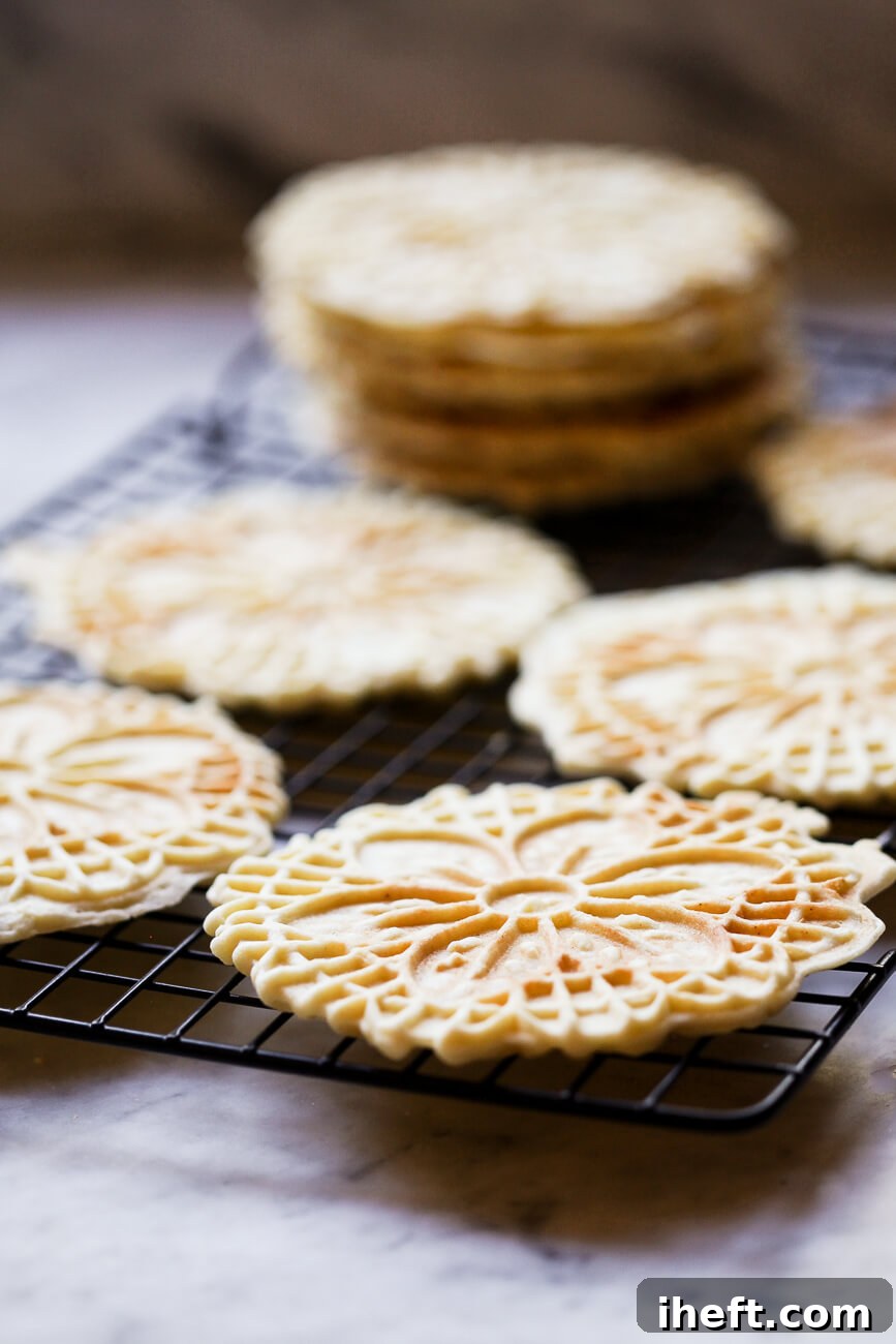 Beautifully freshly cooked pizzelle cookies are carefully arranged on a wire rack to cool and crisp up, sitting on a polished marble countertop.