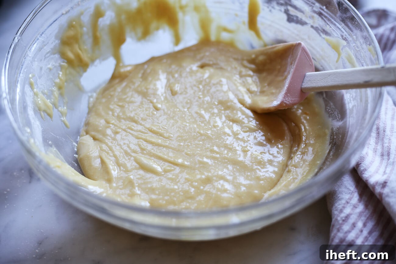 A rubber spatula is stirring the thick pizzelle dough in a mixing bowl.